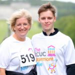 Two people wearing matching event T-shirts, one with race number 519, stand outdoors in a grassy area at Stormont, with blurred trees providing a picturesque backdrop.