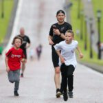 Children running on a road beside adults in Stormont Park, with one boy looking determined in the foreground.