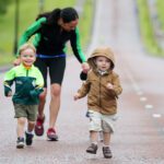 Two young children run on a road with a woman jogging behind them under the cloudy skies of Stormont.