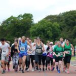 A group of people participating in the Stormont run, wearing numbered bibs, race along a tree-lined road.