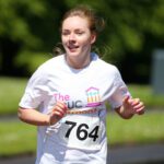 Runner wearing a white shirt with number 764, racing through the scenic paths of Stormont in an exhilarating outdoor event.