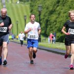 Runners zip down the paved road at Stormont, wearing numbered bibs, as trees and spectators line the bustling race route.