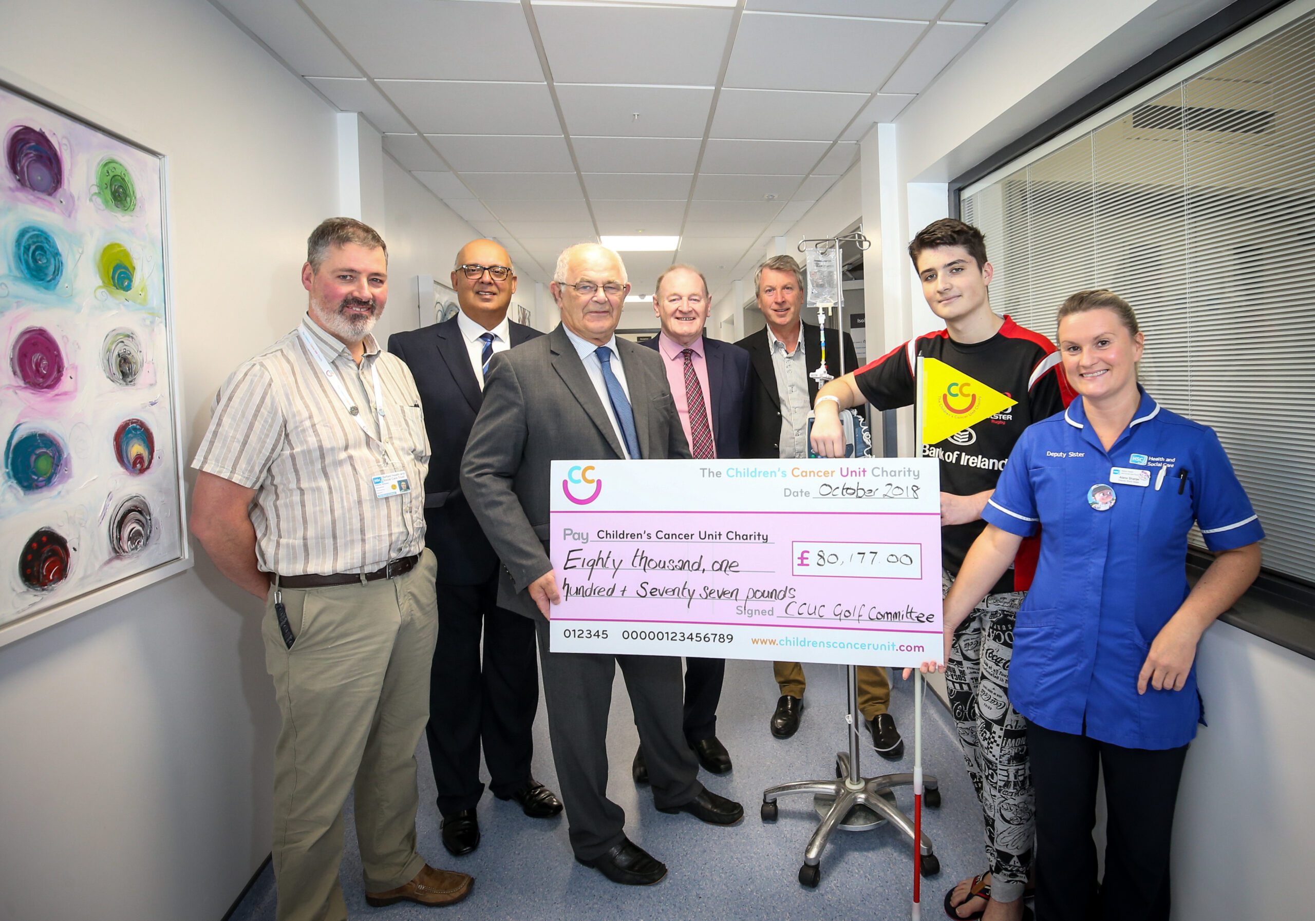 A group of people stands together, holding a large check for £80,177.03 from "The Children’s Cancer Unit Charity," dated 26 October 2019. The business community has clubbed together to support this remarkable cause.