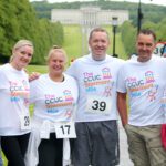 A group of six people in white T-shirts, emblazoned with "The CCUC Stormont Mile" logo, stand together outdoors. With numbers proudly displayed on their race bibs, they embody the spirit of the renowned Stormont event.
