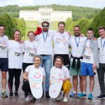 We are a group of eleven people proudly wearing our charity run shirts, posing on a wide path lined with trees. The iconic Stormont building stands grandly in the background, capturing the spirit of our journey together.