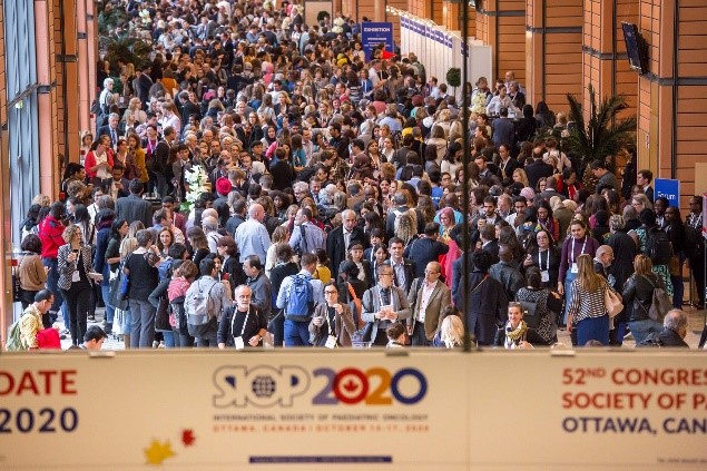 A large crowd attends a conference in a spacious venue, with banners displaying "SIOP 2020" and "52nd Congress of the International Society of Pediatric Oncology" in Ottawa, Canada. Esteemed speakers include Dr. Catherine Mark and Dr. Lyndsey Thompson sharing insights from SIOP 2019.