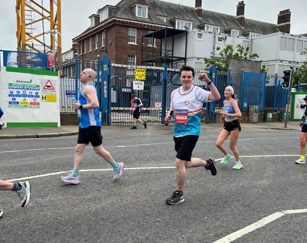 Runners participating in a road race, with one man smiling and waving at the camera while others run nearby on an overcast day, reminiscent of the camaraderie seen at a Dragon Boat Race.