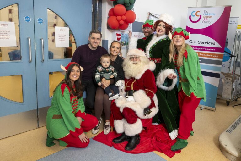 A family with dad, baby and mum are pictured with Santa, Mrs Claus and a group of elves in a hospital.